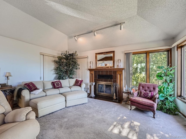 carpeted living room with a textured ceiling, a tiled fireplace, rail lighting, and vaulted ceiling