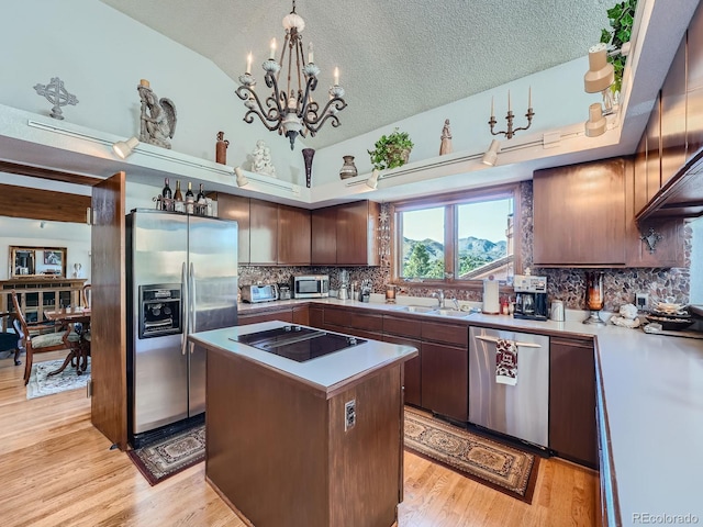 kitchen with a textured ceiling, stainless steel appliances, vaulted ceiling, a center island, and light hardwood / wood-style floors