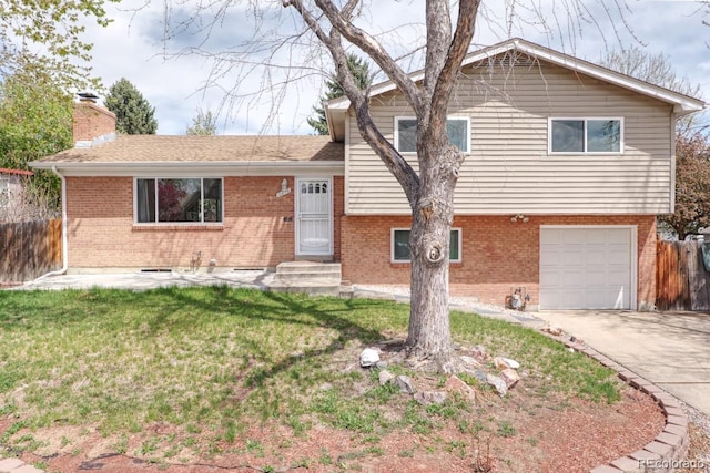 tri-level home featuring fence, an attached garage, a front lawn, brick siding, and concrete driveway