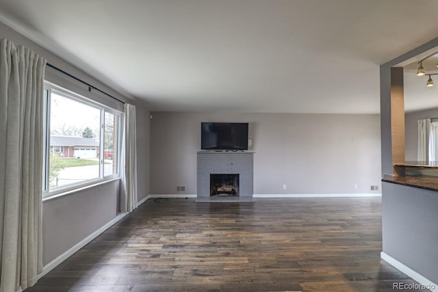 unfurnished living room with baseboards, a brick fireplace, dark wood finished floors, and visible vents