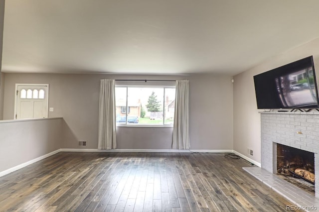 unfurnished living room with baseboards, wood-type flooring, a brick fireplace, and visible vents