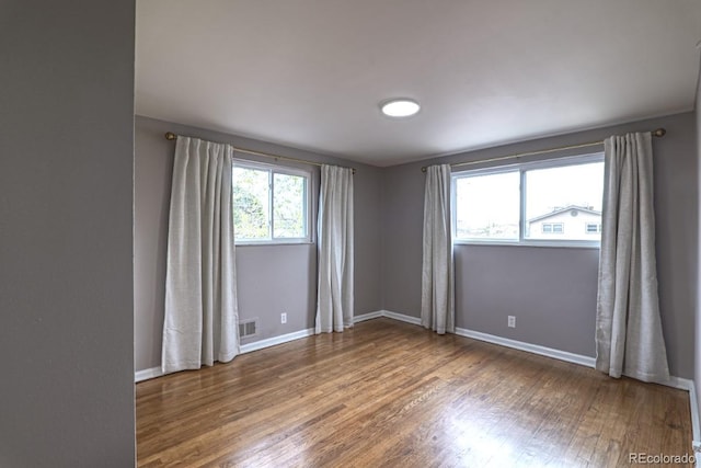 empty room featuring baseboards, wood finished floors, and visible vents