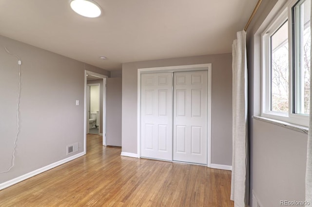 unfurnished bedroom with baseboards, visible vents, light wood finished floors, and a closet