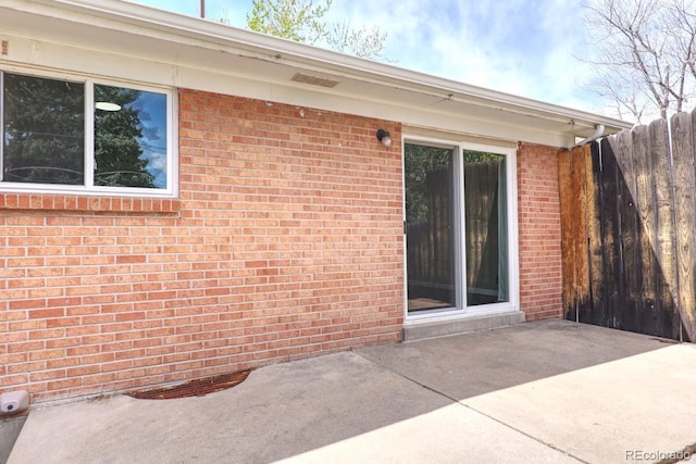 view of exterior entry with a patio, fence, and brick siding