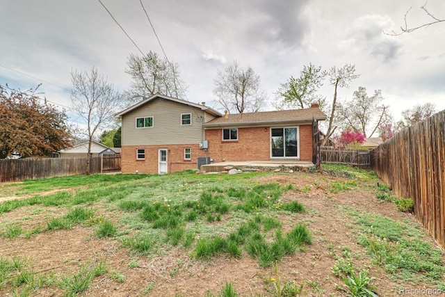 back of property featuring a chimney, central air condition unit, brick siding, a fenced backyard, and a patio