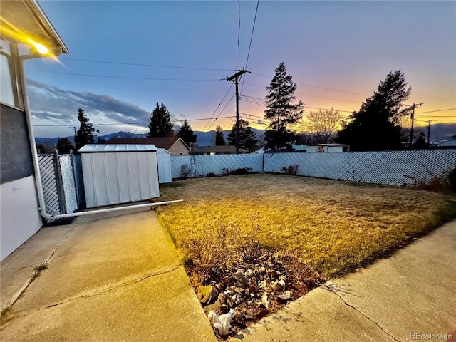 yard at dusk with a fenced backyard, a storage unit, and an outdoor structure