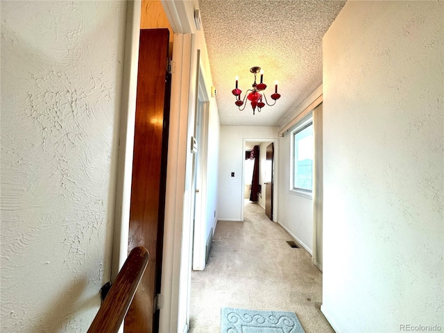 hallway with a textured wall, a textured ceiling, light colored carpet, and visible vents