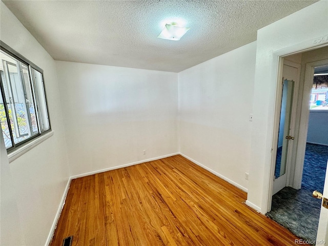 spare room featuring baseboards, visible vents, wood finished floors, and a textured ceiling