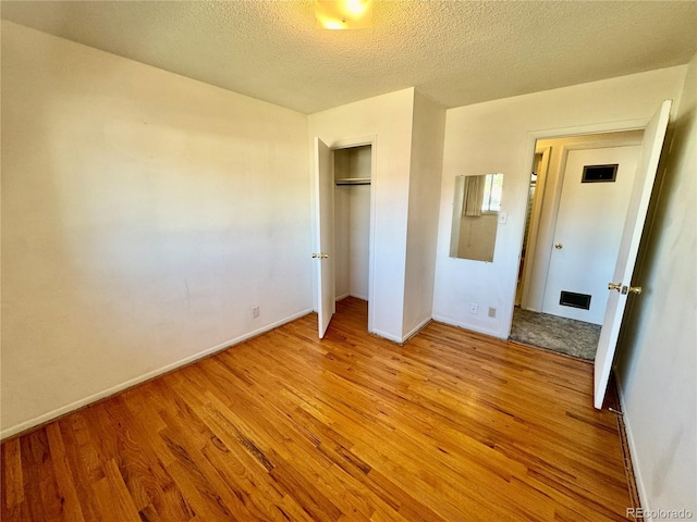 unfurnished bedroom featuring wood finished floors, visible vents, a closet, baseboards, and a textured ceiling