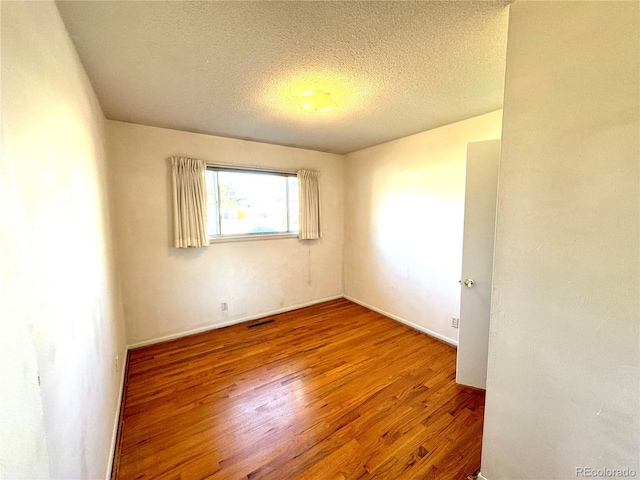 unfurnished room with baseboards, wood finished floors, visible vents, and a textured ceiling