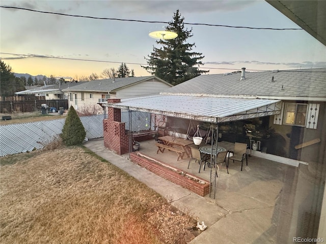 patio terrace at dusk featuring a fenced backyard and a yard