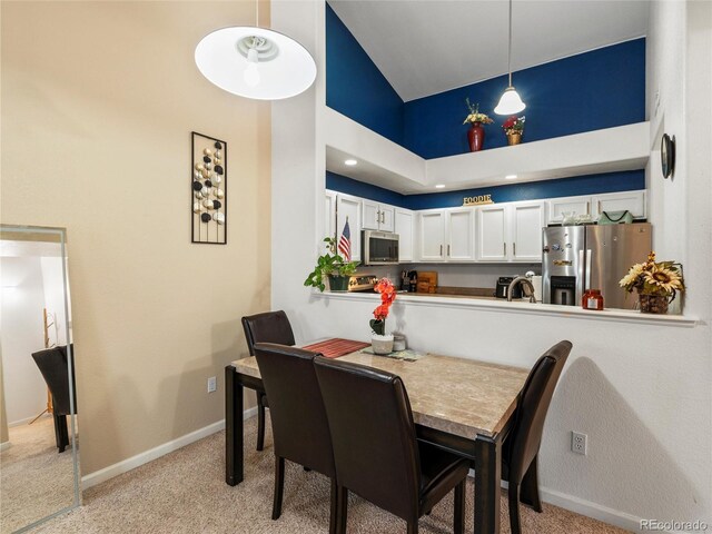 dining room with light carpet, high vaulted ceiling, and baseboards