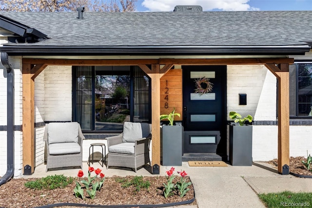 property entrance with covered porch, brick siding, and a shingled roof