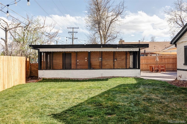 back of property with a chimney, a lawn, a sunroom, brick siding, and fence