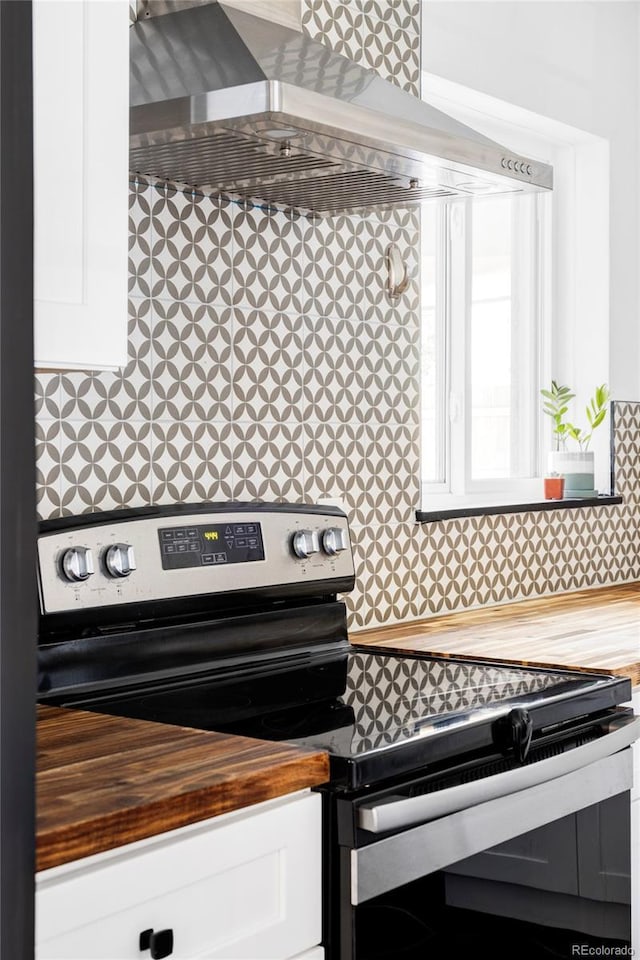 interior details featuring electric stove, white cabinetry, wall chimney range hood, and wooden counters