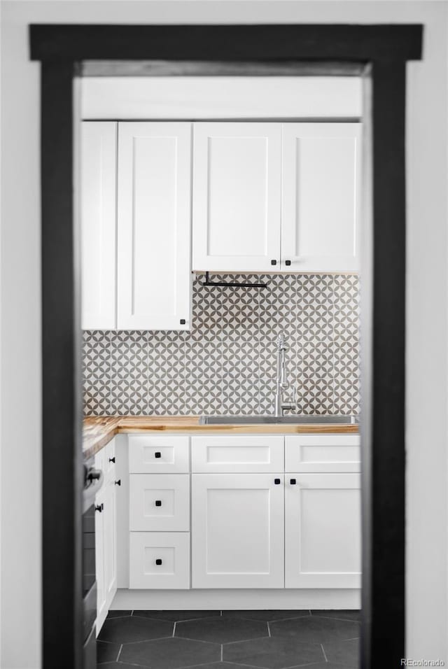 kitchen with a sink, white cabinets, wooden counters, and dark tile patterned flooring