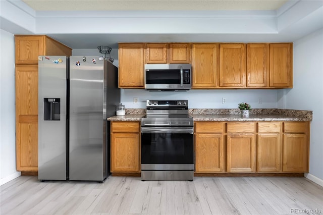 4184 Netherland St, Denver, CO 80249 - kitchen with stainless steel appliances, light wood-type flooring, brown cabinetry, a raised ceiling, and baseboards