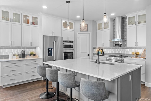 kitchen featuring wall chimney range hood, high quality appliances, tasteful backsplash, a sink, and recessed lighting