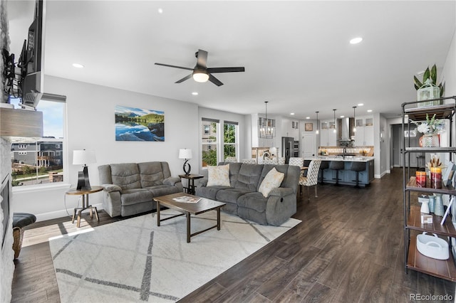 living room featuring a ceiling fan, dark wood-type flooring, recessed lighting, baseboards, and a chandelier