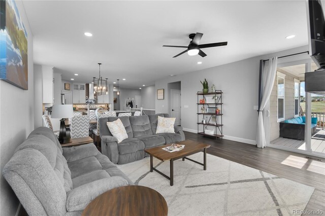living area with dark wood-style flooring, a ceiling fan, a chandelier, recessed lighting, and baseboards