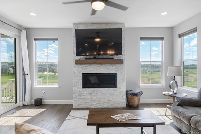 living area with baseboards, wood finished floors, ceiling fan, a stone fireplace, and recessed lighting