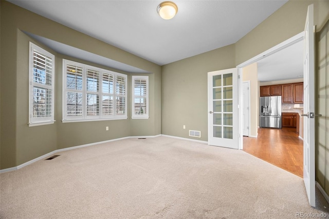 spare room with baseboards, visible vents, french doors, and light colored carpet