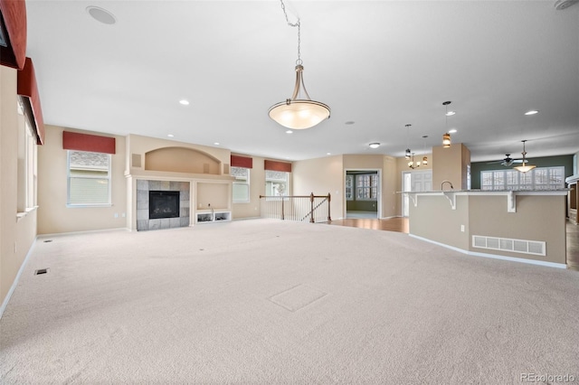 unfurnished living room featuring baseboards, light colored carpet, a tiled fireplace, and visible vents