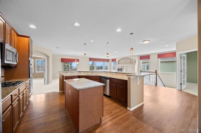 kitchen with a sink, appliances with stainless steel finishes, wood finished floors, and a spacious island