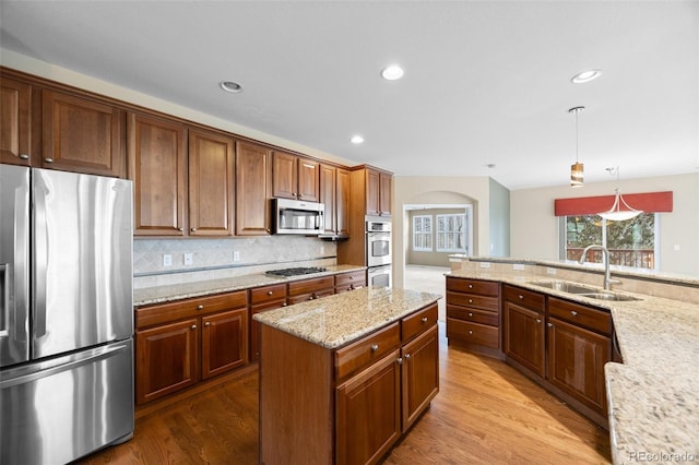 kitchen featuring a sink, arched walkways, stainless steel appliances, wood finished floors, and backsplash