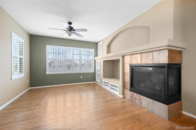 unfurnished living room featuring ceiling fan, wood finished floors, a healthy amount of sunlight, and built in shelves