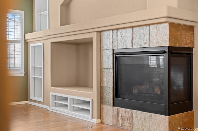 room details with baseboards, built in features, a glass covered fireplace, and wood finished floors