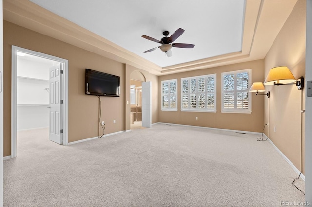 unfurnished living room featuring a raised ceiling, ceiling fan, baseboards, and carpet flooring