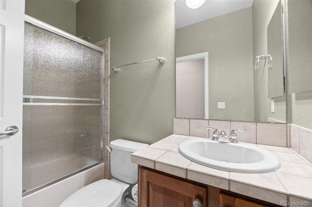 full bathroom featuring vanity, a textured wall, enclosed tub / shower combo, and toilet