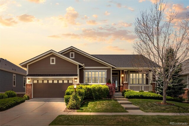craftsman house featuring brick siding, a yard, driveway, and covered porch