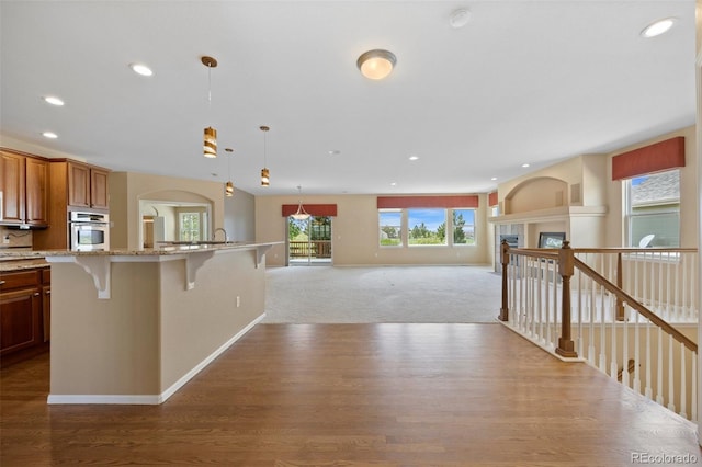 kitchen featuring oven, light stone countertops, recessed lighting, wood finished floors, and a kitchen bar