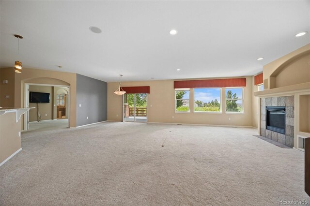 unfurnished living room with light colored carpet, arched walkways, recessed lighting, baseboards, and a tile fireplace