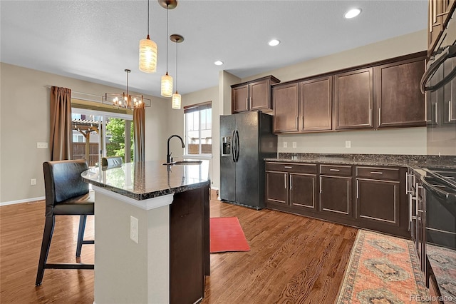 25486 E 4th Pl, Aurora, CO 80018 - kitchen with black fridge with ice dispenser, wood finished floors, dark brown cabinets, a kitchen breakfast bar, and recessed lighting