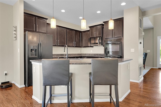 25486 E 4th Pl, Aurora, CO 80018 - kitchen featuring stainless steel microwave, refrigerator with ice dispenser, dark brown cabinetry, wood finished floors, and a breakfast bar
