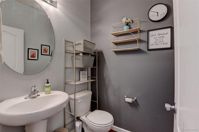 bathroom with a sink, toilet, a textured wall, and baseboards