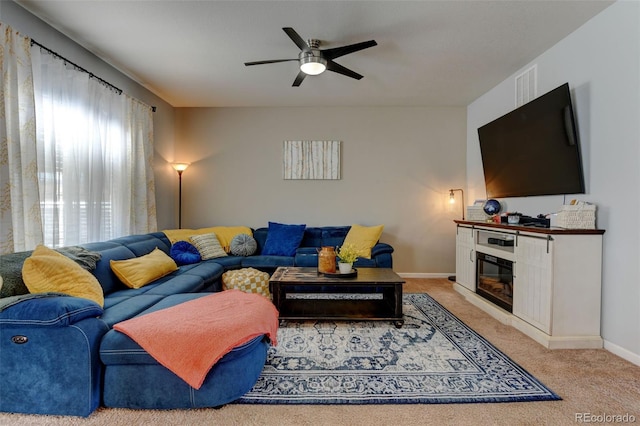 living area featuring a ceiling fan, light colored carpet, baseboards, and a glass covered fireplace