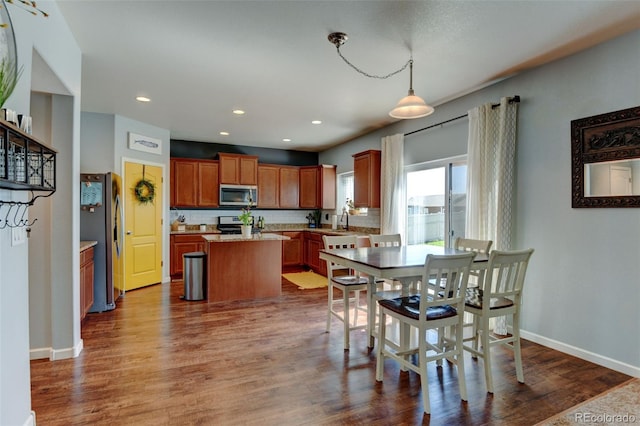 kitchen featuring stainless steel appliances, a kitchen island, dark wood-style flooring, baseboards, and brown cabinets