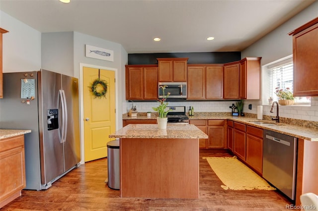 kitchen featuring stainless steel appliances, a sink, light wood finished floors, decorative backsplash, and a kitchen island