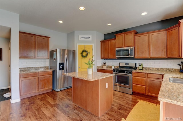kitchen with stainless steel appliances, a center island, tasteful backsplash, wood finished floors, and light stone counters
