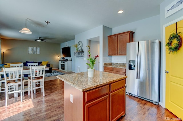 kitchen featuring stainless steel fridge with ice dispenser, ceiling fan, wood finished floors, open floor plan, and a center island