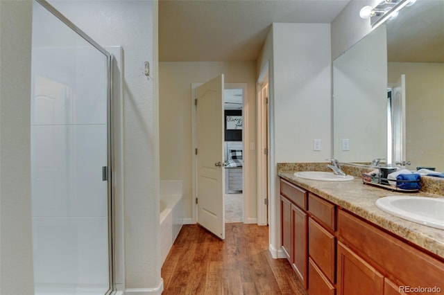 bathroom with wood finished floors, a stall shower, double vanity, and a garden tub