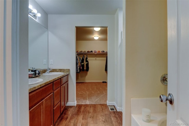 bathroom with wood finished floors, double vanity, a walk in closet, and a bath
