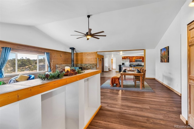 interior space featuring a wood stove, ceiling fan, dark wood-type flooring, vaulted ceiling, and appliances with stainless steel finishes