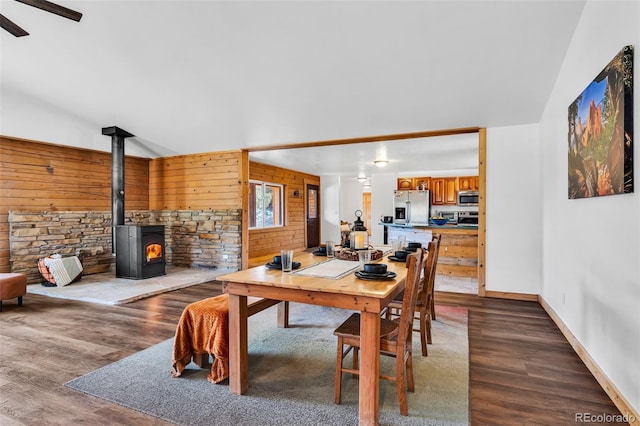 dining room featuring vaulted ceiling, ceiling fan, hardwood / wood-style floors, a wood stove, and wood walls