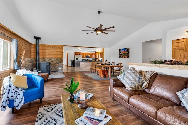 living room with a wood stove, ceiling fan, dark hardwood / wood-style flooring, vaulted ceiling, and wooden walls