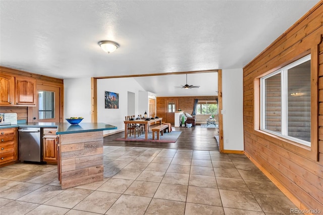 kitchen featuring stainless steel dishwasher, ceiling fan, light tile patterned floors, and brick wall